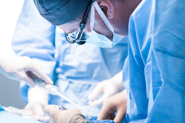 A male dentist in uniform perform dental implantation operation on a patient at dentistry office.