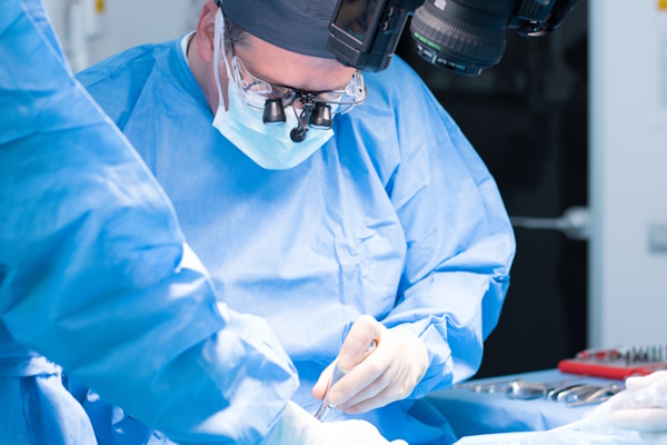 A male dentist in uniform perform dental implantation operation on a patient at dentistry office.